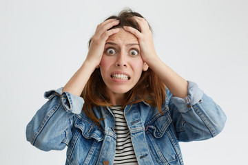 Portrait of shocked terrified woman with dark eyes popped out clenching her teeth holding hands on head looking in despair into camera isolated over white background. Woman having frustration