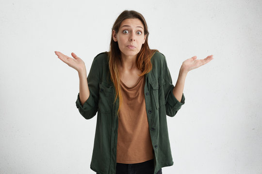 Clueless puzzled woman with widely opened eyes having hesitation shrugging her shoulders expressing uncertainty. Facial expressions, life perception and attitude concept. Nobody cares about it