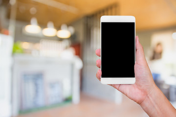 hand holding white mobile phone with blank black screen on blurred cafe.