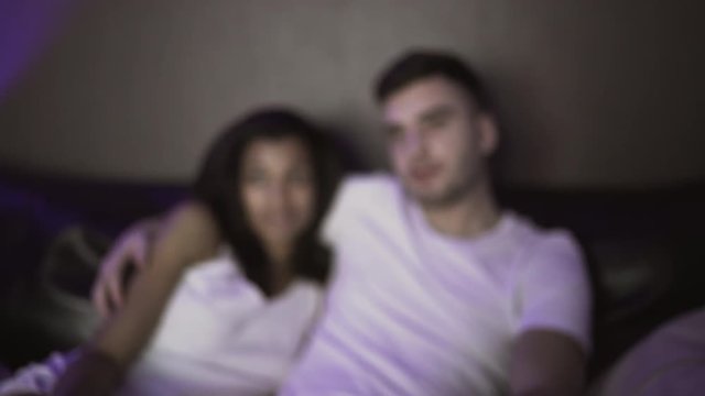 Loving couple sitting on the couch and watching tv at home at night time. 4K