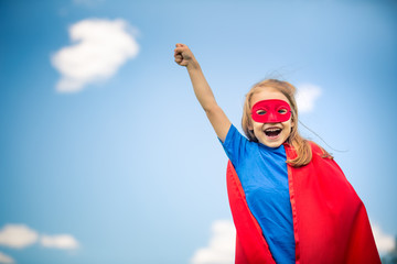 Funny little girl playing power super hero over blue sky background. Superhero concept.