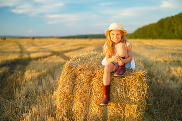 Little girl in a field with hay rolls at sunset
