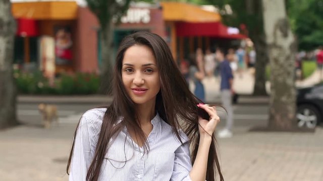 Close-up face of a beautiful brunette with long hair in a city Park. On the background of blurred people.