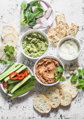 Vegetarian dip table. Eggplant, harissa, walnuts dip, broccoli dip, soft tofu and fresh vegetables on a light background, top view. Flat lay