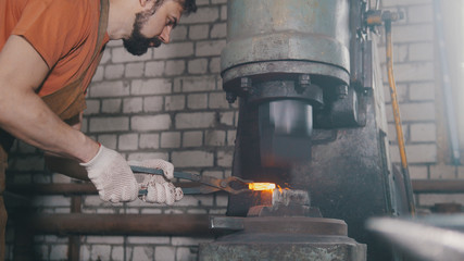 Man blacksmith forges the metal at the mechanical hammer