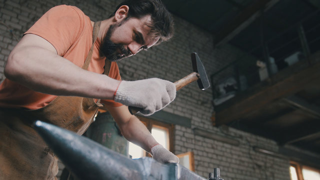 Muscular blacksmith in forge hammering steel products