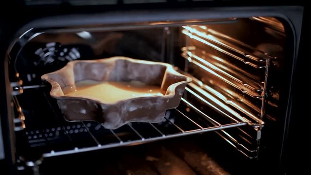 The woman puts the cake in the oven