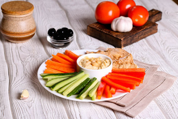 hummus served in a bowl with fresh vegetable sticks and whole grain crackers