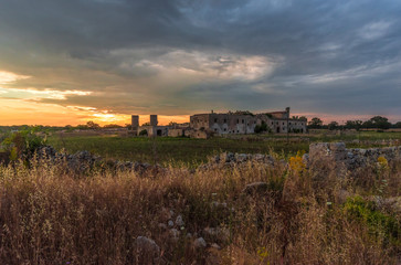 Fototapeta na wymiar Puglia (Italy) - Wind farm with rock ruins, wind turbines and bales of hay at sunset