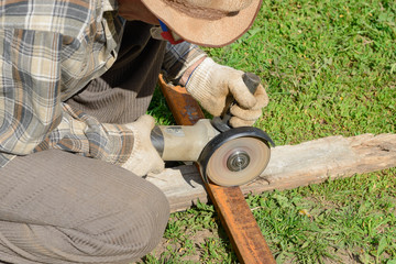 The worker saws a metal profile in the summer green yard
