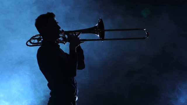 Man in silhouette playing on trombone. Smoky studio, slow motion