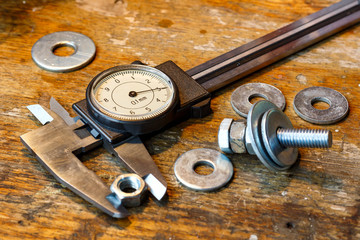 Obraz na płótnie Canvas Slide caliper with round scale and bolt with nuts on the workbench in workshop