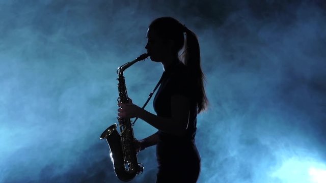 Silhouette musician female playing on saxophone. Smoky studio, slow motion