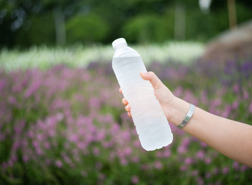 Woman hand holding bottle of water on nature background.