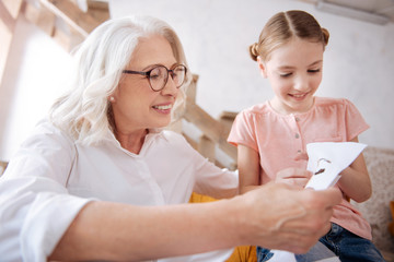 Joyful happy woman looking at her granddaughters embroidery