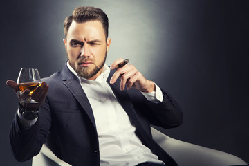 Handsome man with cognac glass in hand smoking cigar