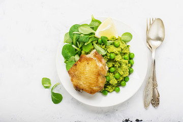 Easy healthy lunch: chicken thigh with mashed green peas and corn salad on a light background. Top view