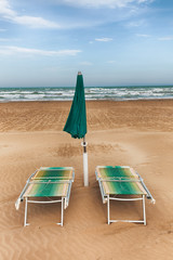 Beach chairs and green umbrella on sand beach in Vieste, Gargano Puglia, Italy