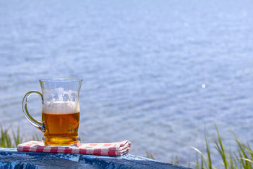 Mug of beer on the table by the lake