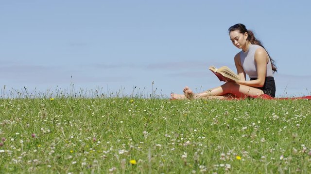 Young woman sits on a blanket reading outdoors in the sunshine, with space for text
