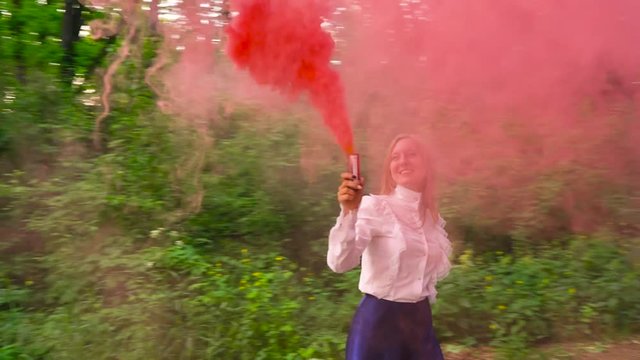 Woman in beautiful clothes runs through the forest waving colored smoke