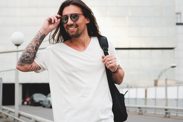 Stylish hipster model with long hair lifestyle in the street. Dressed in a white T-shirt and torn...
