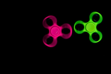 Pink and green Fidget Spinner in black background for stress release during work.