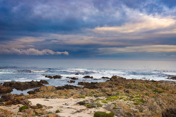 Rocky coast line on the ocean at De Kelders, South Africa, famous for whale watching. Winter season, cloudy and dramatic sky.