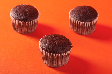 A group of chocolate cupcakes on orange background.
