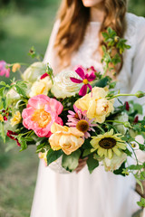 wedding, floral design, fashion, celebration concept - beautiful bouquet of ornamental flowers tender avalanches, peonies and marsala colored carnations in hands of bride in white dress