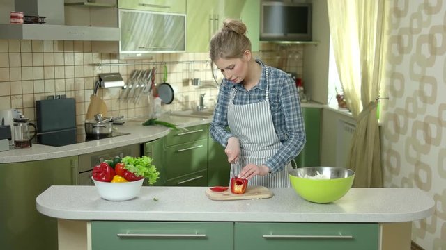 Woman cutting paprika. Lady in apron, kitchen. Make salad taste better.