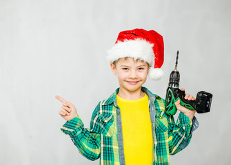 Boy in a red christmas hat with a drill points to empty space