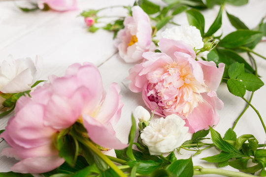 Close up of pink and white flowers on wooden table. Peonies and wild roses. High key, copy space.