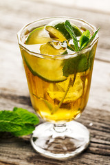 Tasty fresh refreshing summer tea drink with ice, cold tea, lime and mint in glass on wooden background. Closeup.