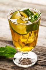Tasty fresh refreshing summer tea drink with ice, cold tea, lime and mint in glass on wooden background. Closeup.