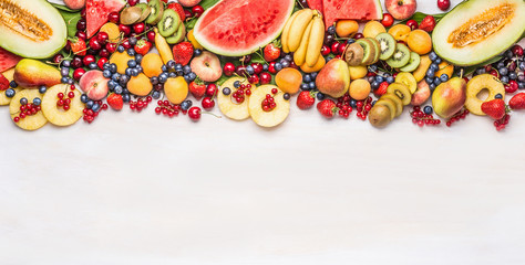 Variety of colorful organic fruits and berries on white table background, top view, border. Healthy food and vegetarian eating concept