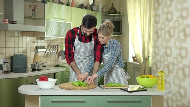 Man and woman cutting lettuce. Tablet in the kitchen.