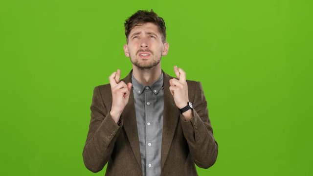 Businessman crosses his fingers on both hands in the hope of success. Green screen