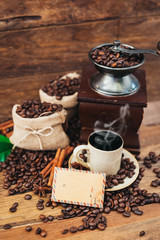 Cup of coffee with sack full of roasted coffee beans and coffee mill on wooden table