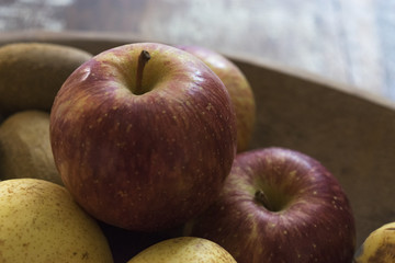 Real organic red apples with other fruits in a wooden tray.