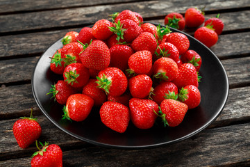 Fresh strawberries in a black plate on old wooden table
