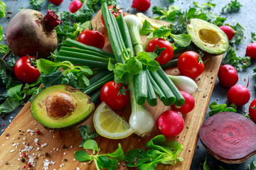 Seasonal vegetables ingredient for salad, red radish, tomatoes, spring onions, beetroot, lemons and avocado on oak cutting board with sea salt and corn peppers
