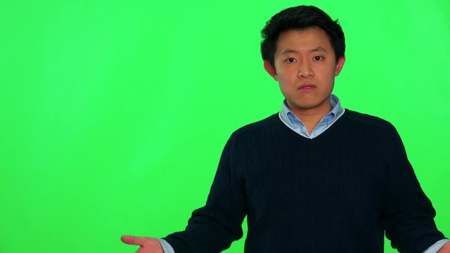A young Asian man looks at the camera and gesticulates in frustration - green screen studio
