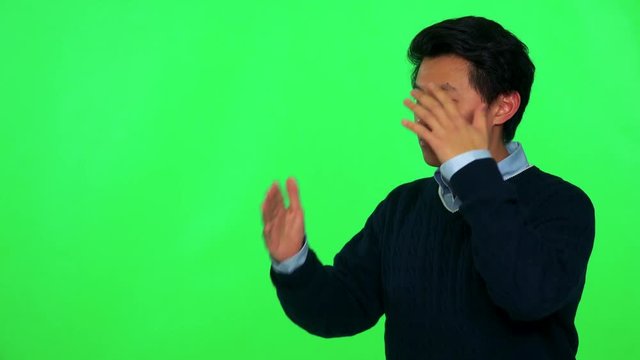 A young Asian man is angry at something off the camera, frowns and waves fists - green screen studio