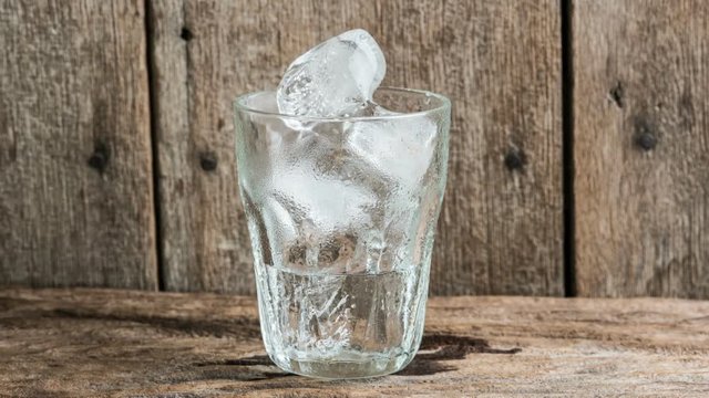  Time lapse Ice in the glass is melting and wooden table background