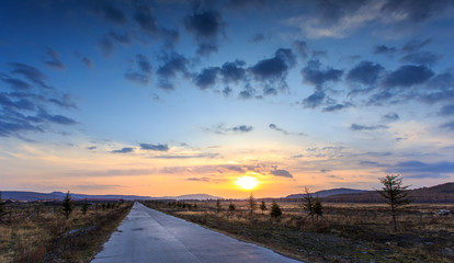 Sunset over yellow grassland and empty road