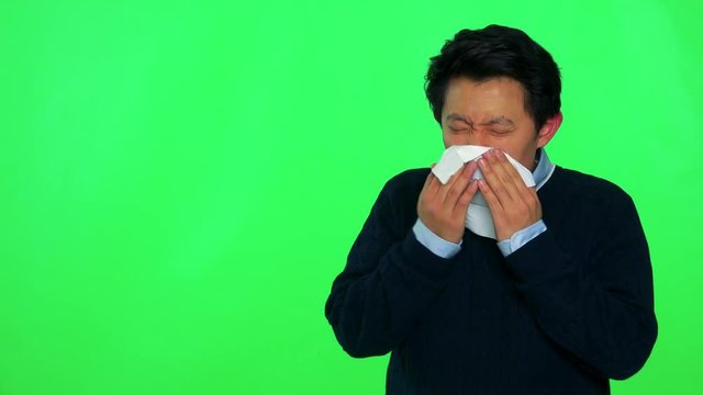A young Asian is sick and blows his nose into a paper tissue - green screen studio