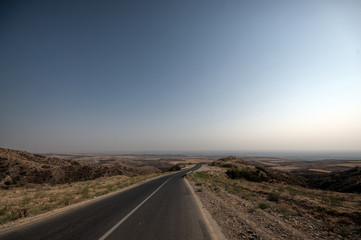 Road vanishing to the horizon under sun rays coming down trough the dramatic stormy clouds. Sunset at the mountain road. Azerbaijan, Ganja