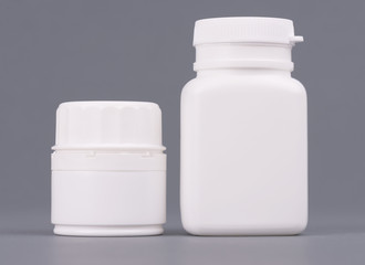 Blank big and medium size medicine white plastic packaging bottles for cosmetics, vitamins, pills or capsules. Packaging on gray background