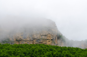 Fototapeta premium Haze fog over the rocks. Cloud over the mountainin Caucasus. Green leaf forest. Mezmay and Guamka